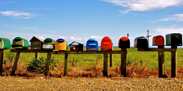 Postkasser på landsbygda i ulike farger og med ulik form. Foto