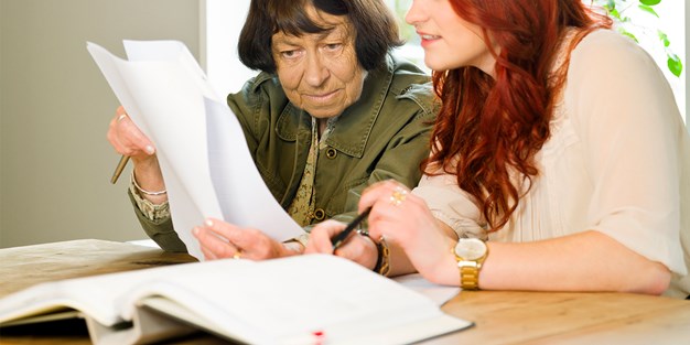 Yngre rödhårig kvinna och äldre kvinna som bläddrar bland papper. Foto