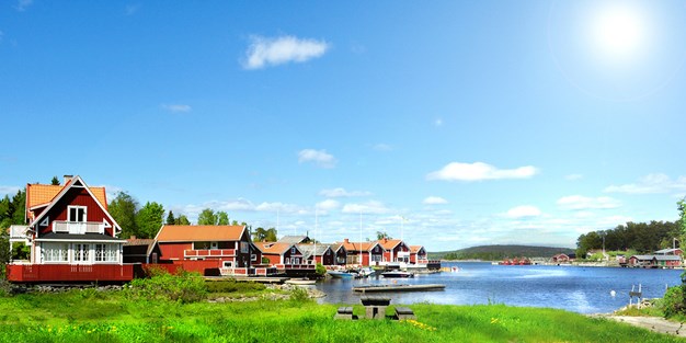 Röda stugor vid en sjö i sommarsol. Foto