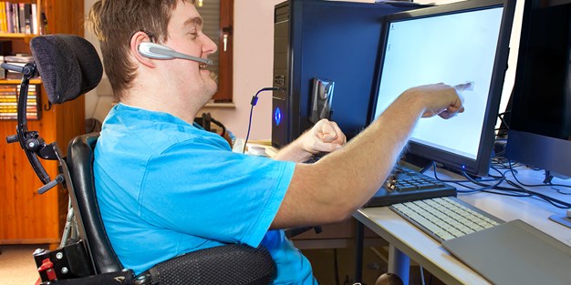 A person in a wheelchair using a computer. Photo.
