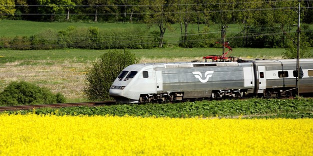 Ett SJ-tåg som åker över ett sommarlandskap. Foto