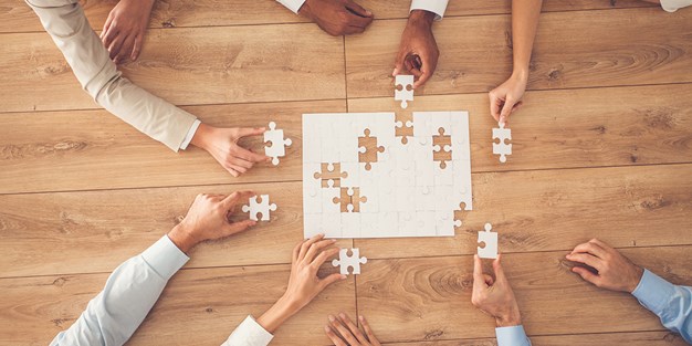 People around a table playing with a puzzle. Photo.