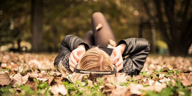 En ungkvinna som ligger på rygg i ett höstigt landskap med hörlurar. Foto