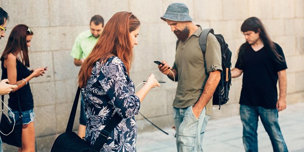 Flera personer som använder smartphones på en gata. Foto
