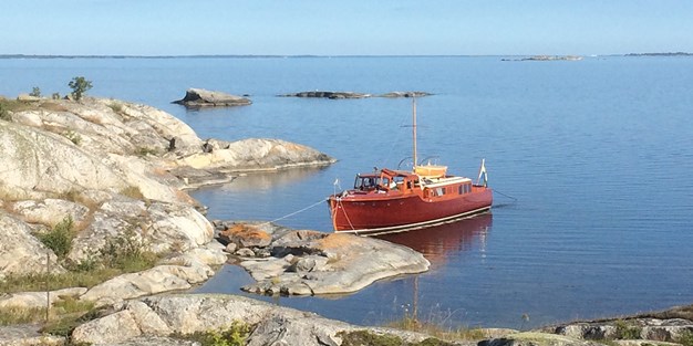 En båt som ligger för ankar vid några klippor. Foto