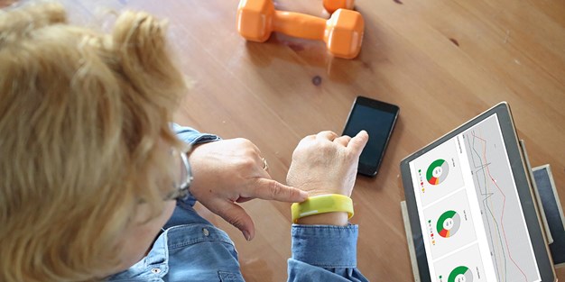 Person seen from above touching its digital device on the arm and a dumbbell is on the floor, photo.