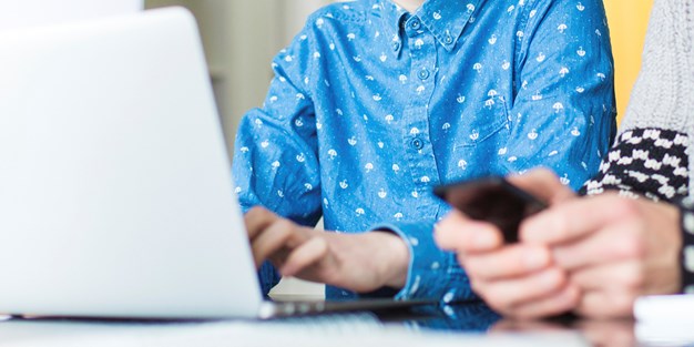 En kvinne i blå skjorte foran en PC. Foto