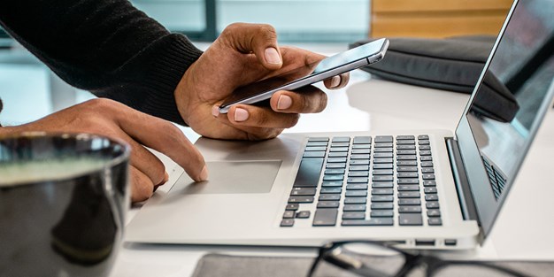 En person som använder en laptop och en smartphone. Foto