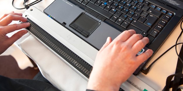 En person som använder en punktskriftsläsare vid datorn. Foto