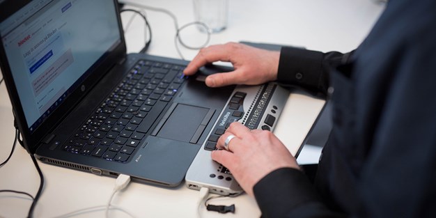 A person using a screen reader and a Braille display on a computer. Photo.