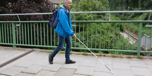 En synshemmet person som går med en hvit stokk. Foto